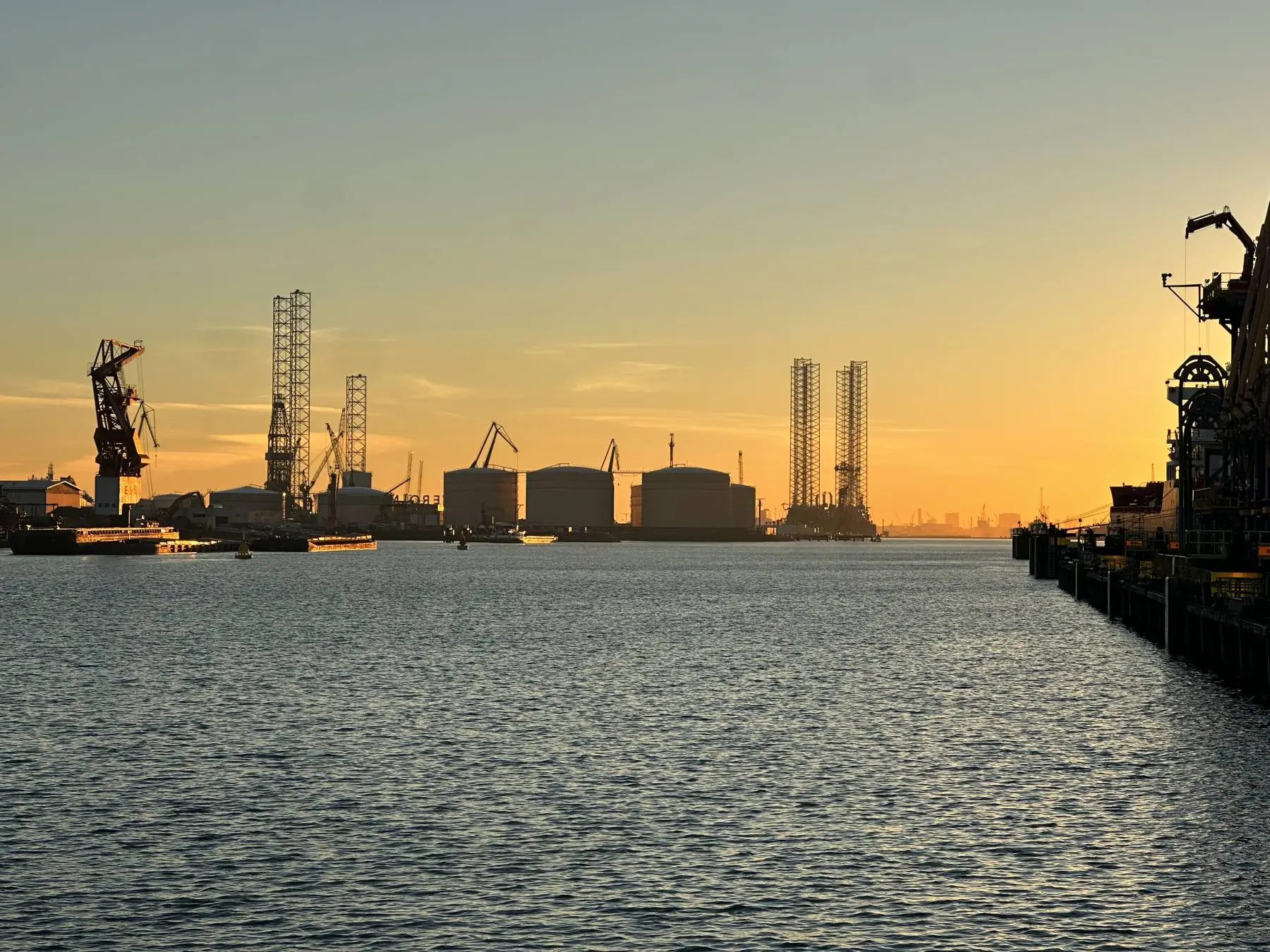 Port z dźwigami stoczniowymi i zbiornikami o zachodzie słońca.