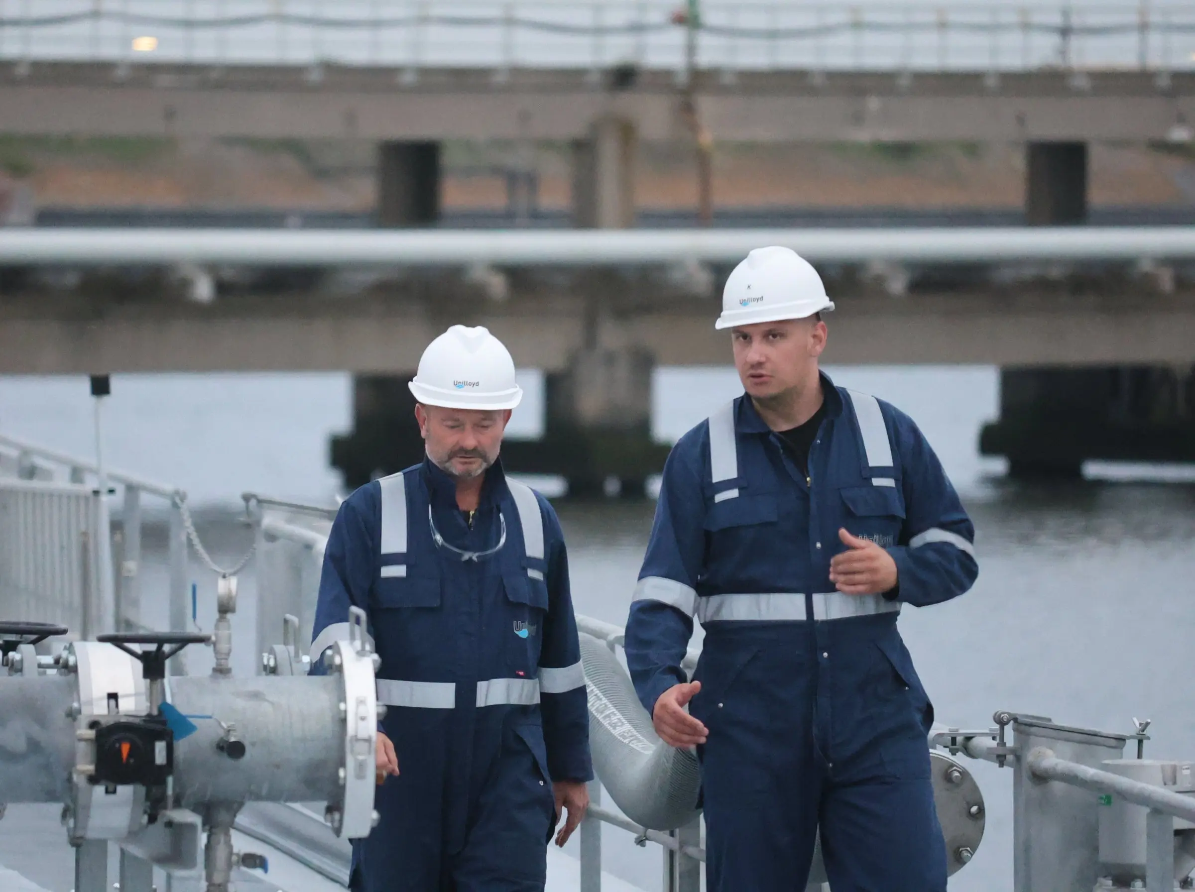 Two crew members in hard hats on the deck of a tanker.